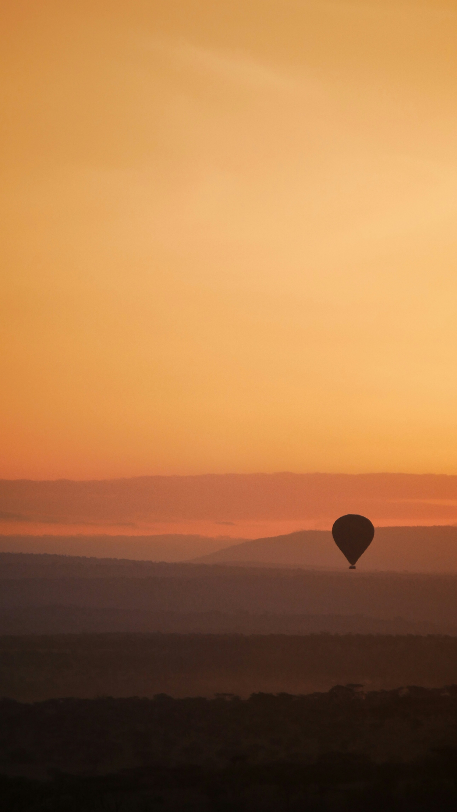 A Single Hot Air Balloon Flies In An Orange Dusty Sky In The Desert Hilly Landscape