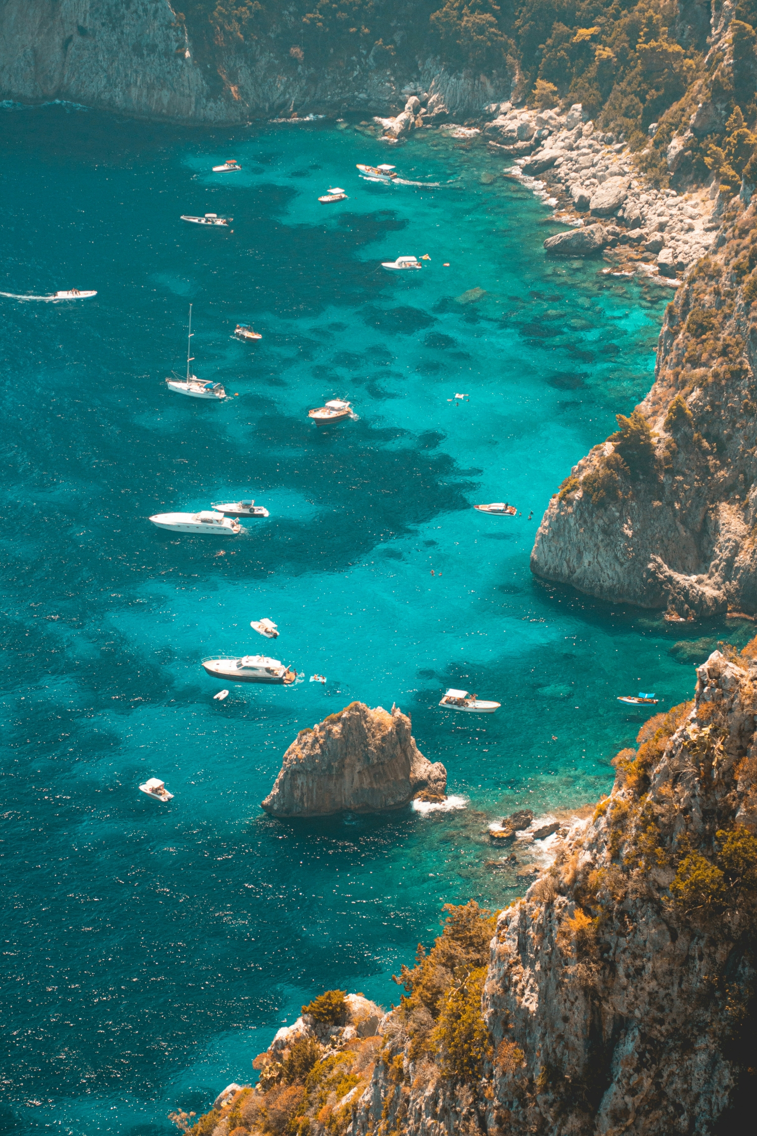 Beautiful Vibrant Blue Bay With Tall Rocks And Cliffside With Luxury Boats Docked In The Water