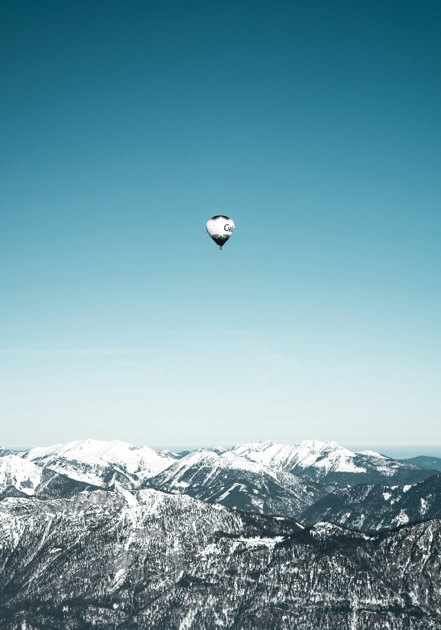 Singular Hot Air Balloon Flies Alone In The Sky Over Snowcapped Mountains wallpaper for Apple iPhone, Apple Watch, Mac, iPad and Apple Watch