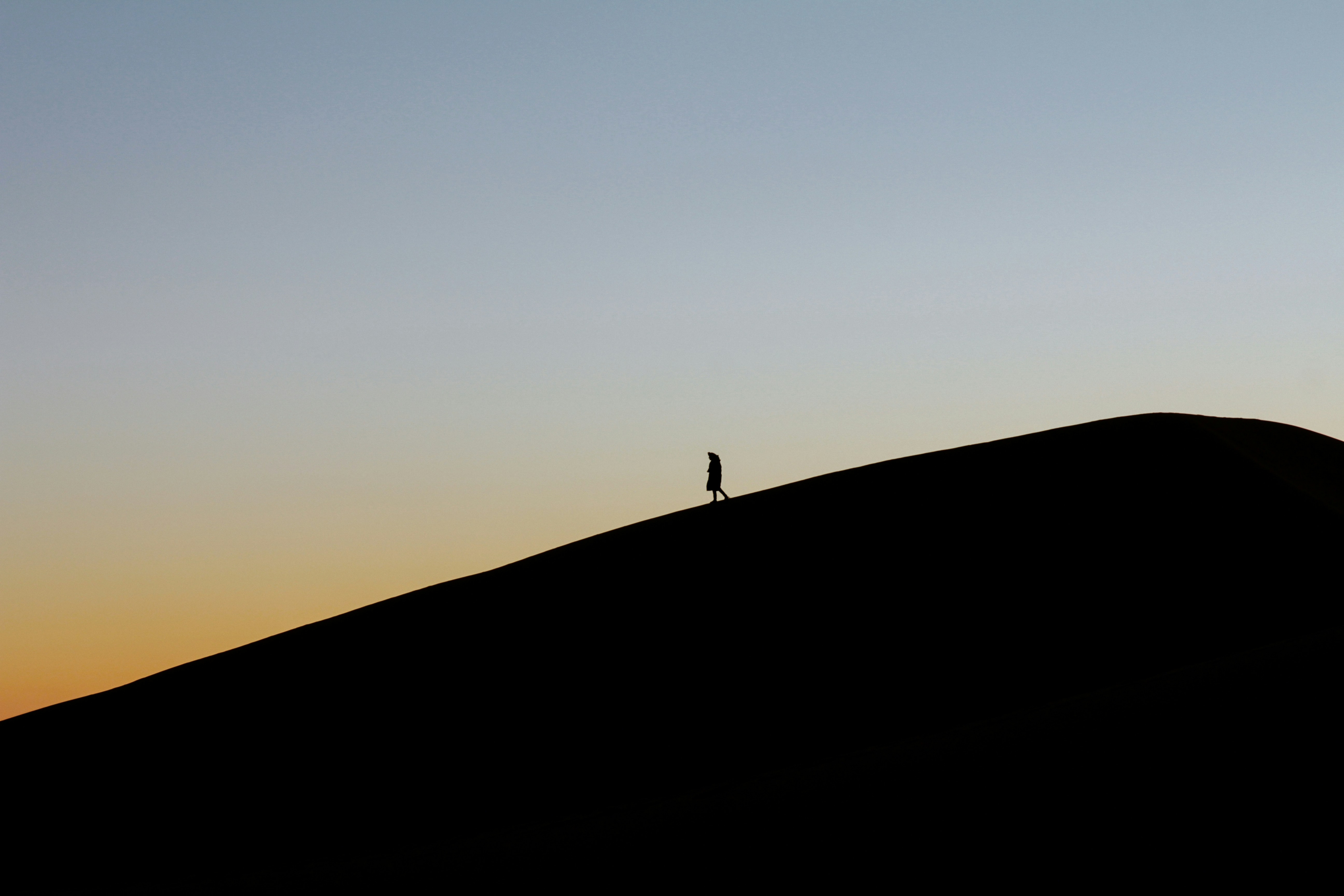 Silhouette Of A Woman Walking On A Sand Dune At Sunset