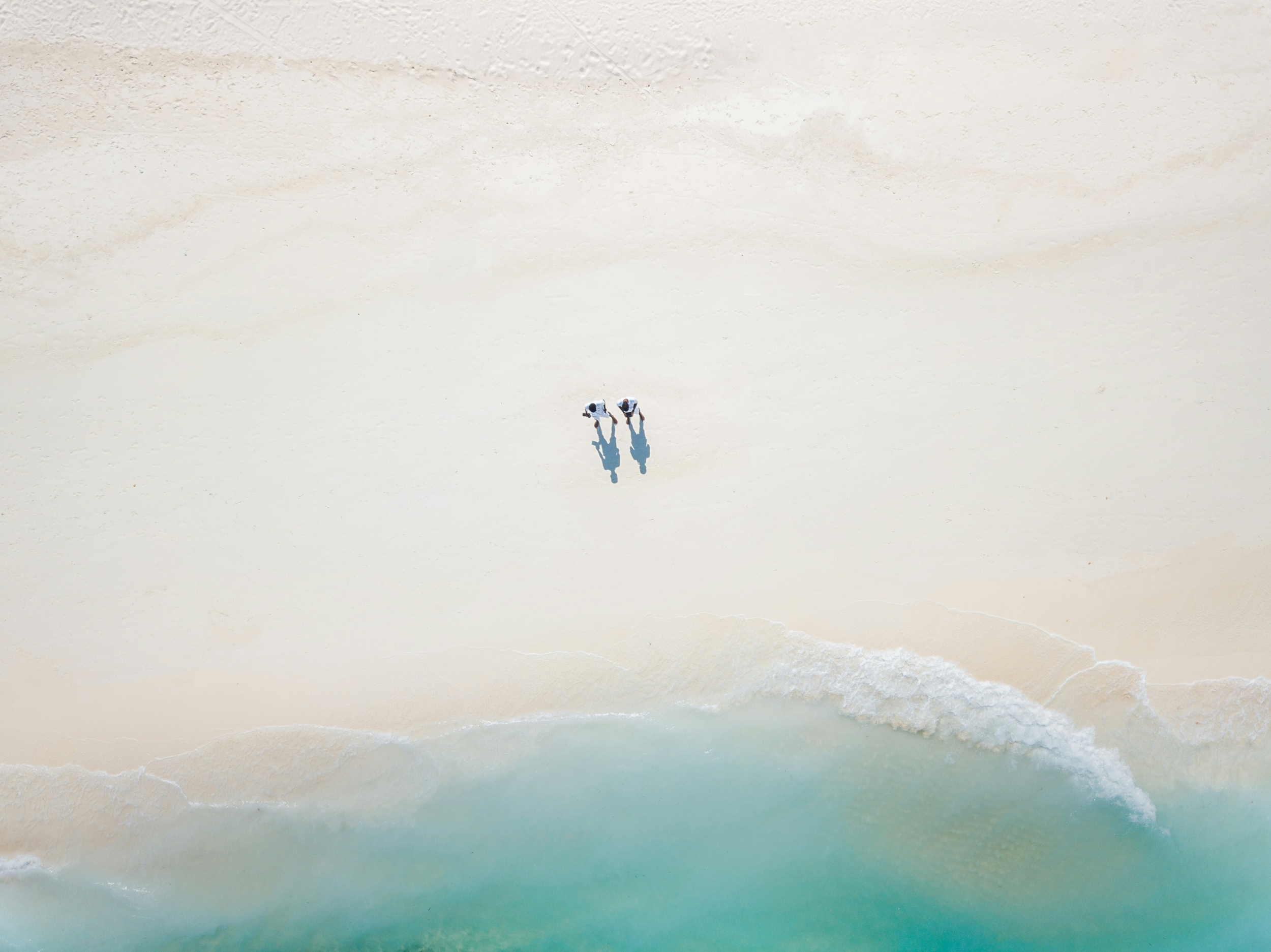 Two People Walking On A Crystal Clear Water Beach From Above wallpaper for Apple iPhone, Apple Watch, Mac, iPad and Apple Watch