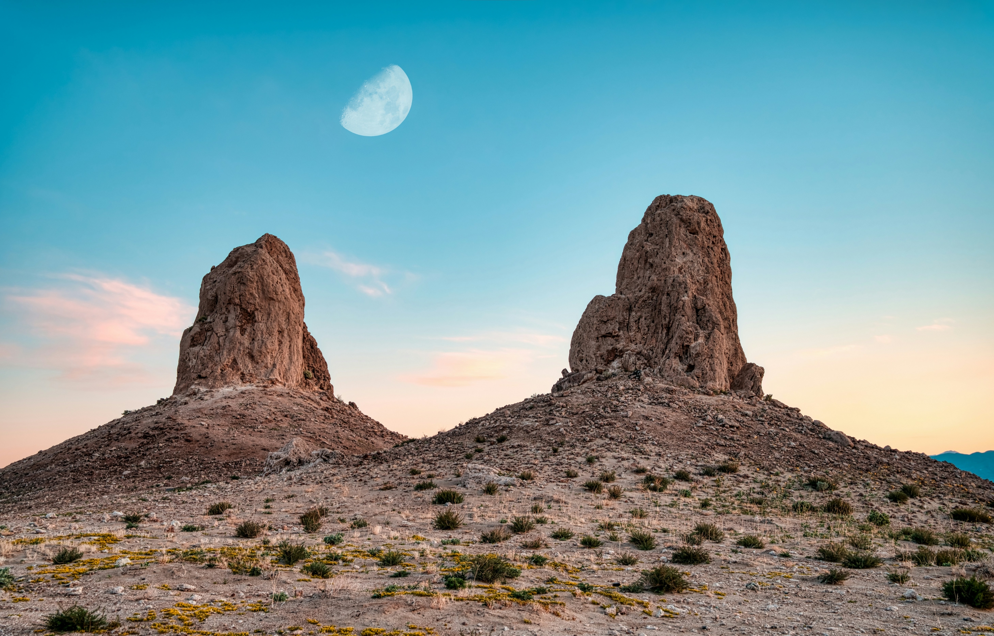 Two Unique Rock Formations In The Desert With Sunset And Moon